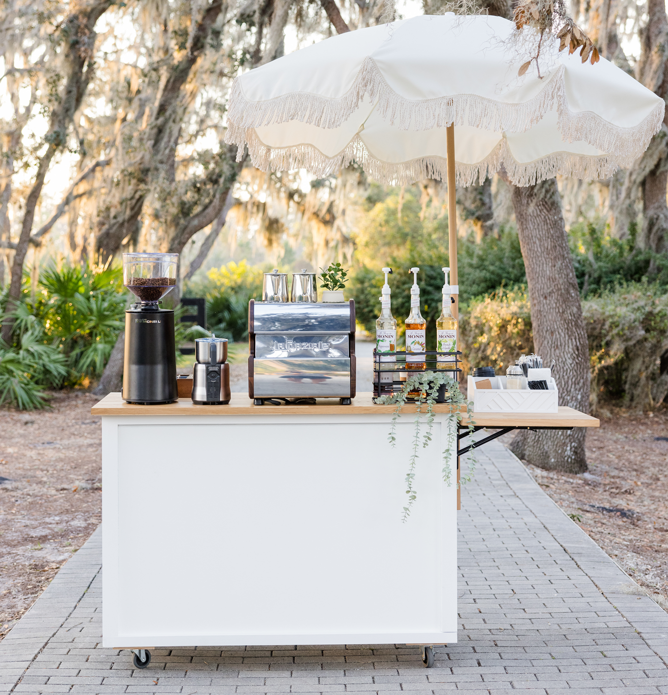 Elegant mobile coffee cart setup with espresso machine, grinder, and syrup dispensers under a decorative umbrella
